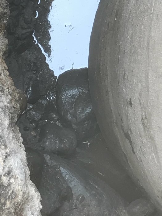 Stenar och grus under en stor betongcylinder med en vattenpöl som reflekterar ljuset.