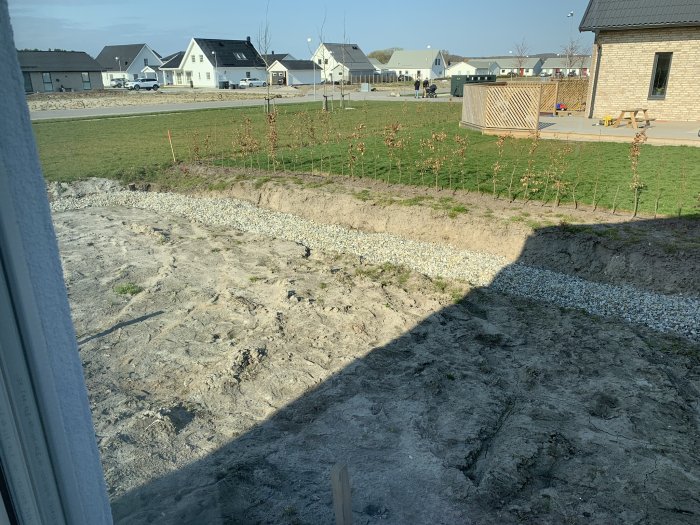 Nydränerad trädgård med markduk, makadam och bar jord, intill villaområde.