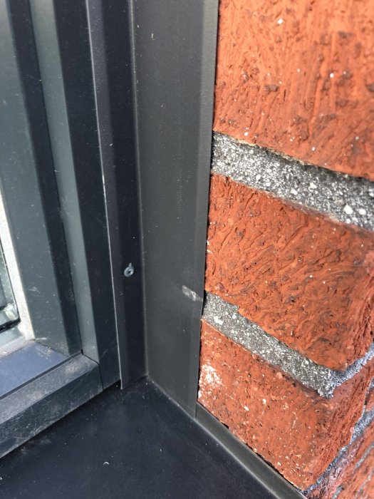 Repat och bucklat montage av svart plåt vid röd tegelvägg och fönsterkarm.