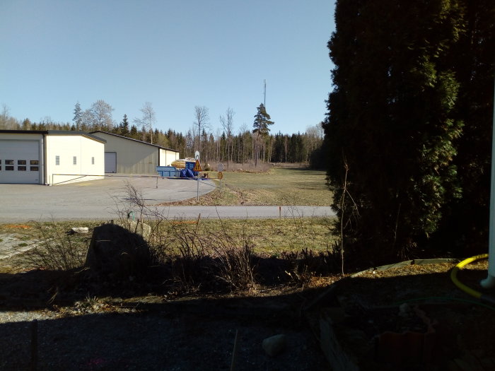 En person skrapar fönster på en stege bredvid en byggnad, med en klarblå himmel och skog i bakgrunden.