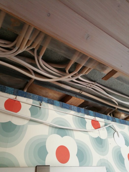 Elektriska kablar dras längs takbjälkar över en vägg med retrotapet i ett pågående renoveringsprojekt.
