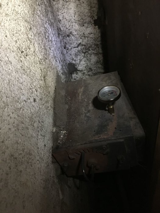 Termometer på en gammal pelletspanna som visar 40-50 grader i en mörk pannrumsmiljö.