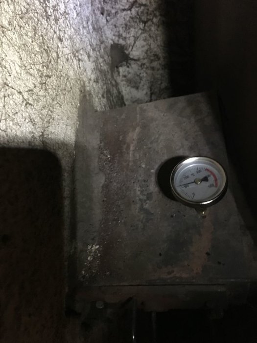 Pelletspanna med termometer som visar runt 40-50 grader i ett mörkt utrymme.