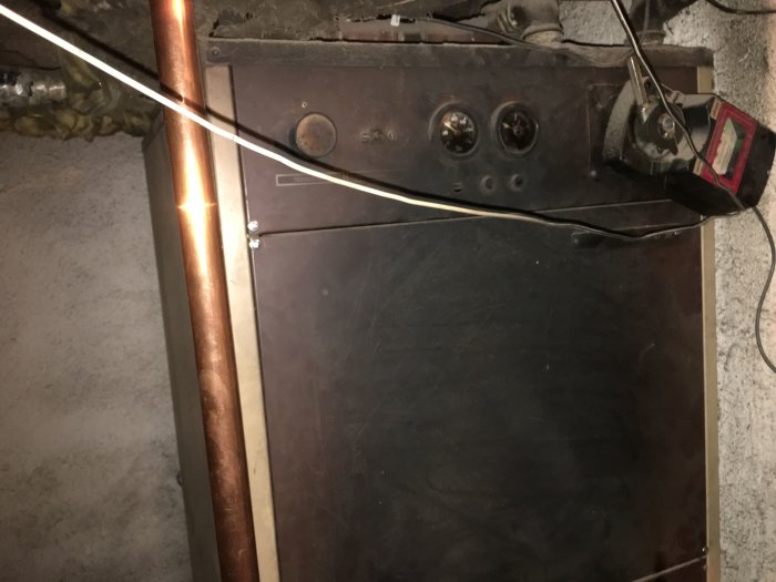 En mörk, dammig panna för uppvärmning med pellets i ett hus, synliga rör och termostat.