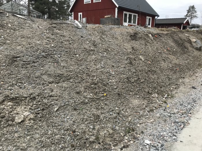 Söndergrävd slänt av grus och jord framför ett rött hus efter vägarbete.