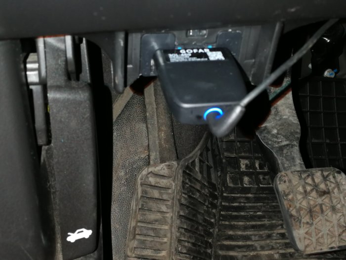 GOFAR-enhet ansluten i en bil med ett blått ljus som indikerar drift, monterad vid förarsidans pedalområde.