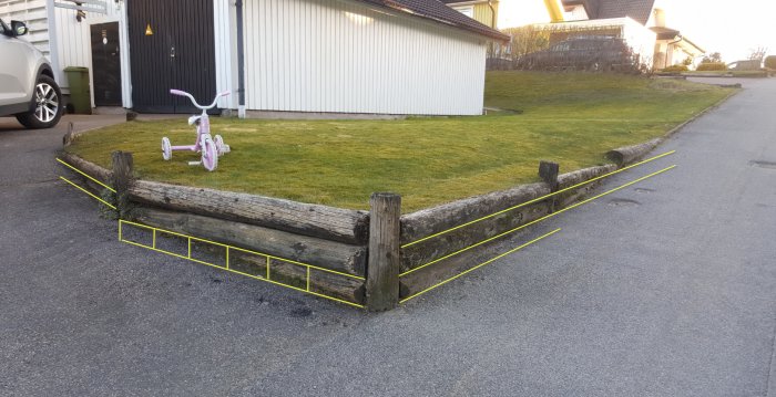 Gamla slipers som bildar en stödmur vid en sluttande uppfart, markerad för byggålning, med ett rosa barntrampcykel i förgrunden.