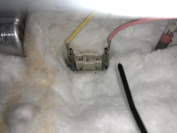 Isolerad elanslutning med gula och rosa kablar som syns genom fiberglasisolering.