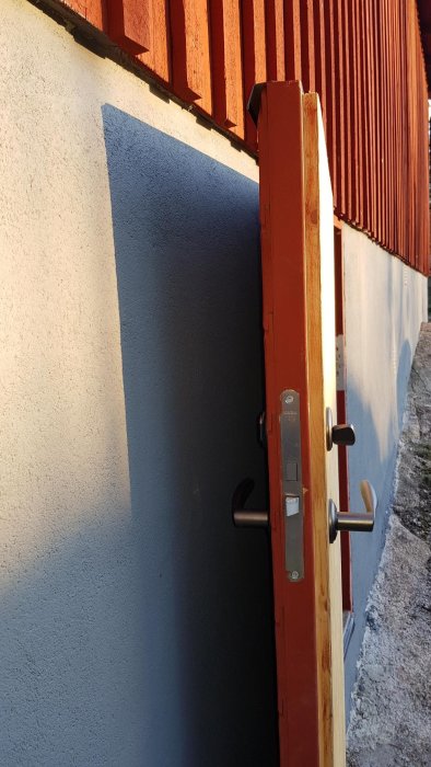 Källardörr öppen nästan 180 grader mot en putsad vägg med dörrhandtag som nuddar putsen.