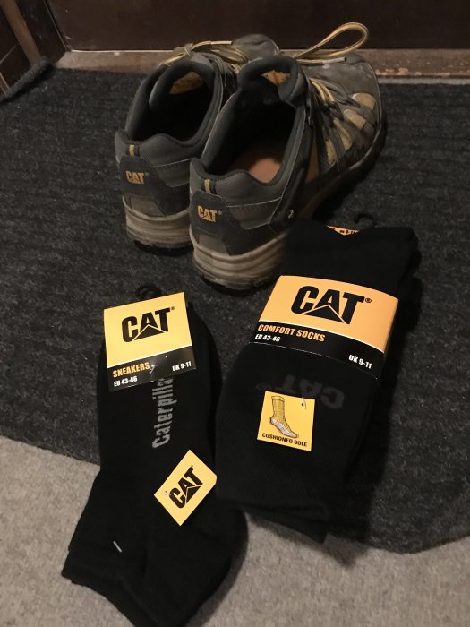 CAT-arbetsskor och nya matchande CAT-sockar i förpackningar på en matta.