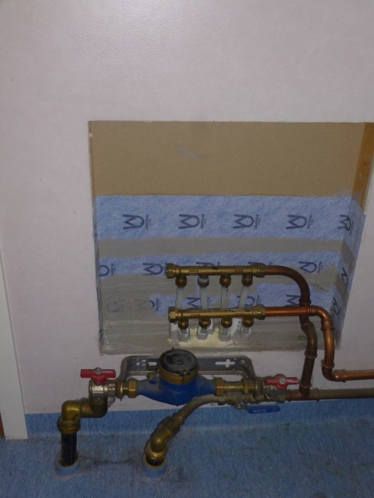 Vägg med VA-installationer inklusive kopparledningar och en central ventilsamling, med skyddande musband och klämringstätningar.