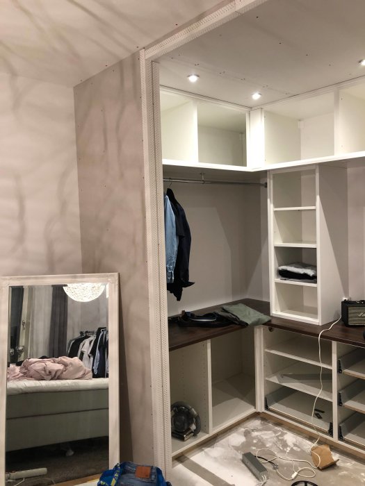 Nybyggd walk-in-closet under konstruktion med vita hyllor och klädstång, byggmaterial och verktyg synliga.