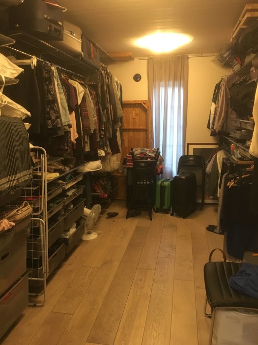 Ett klädfyllt walk-in-closet med Elfa hyllsystem och diverse föremål som resväskor, lakan och en strykbräda.