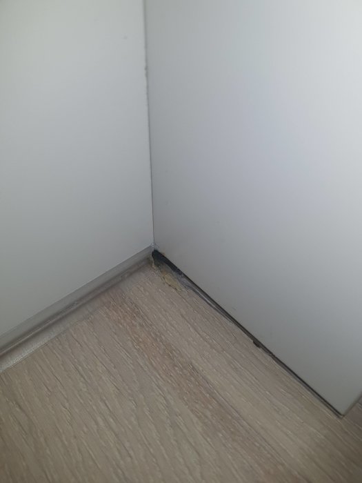 Överskott av transparent silikon och slarvigt finishat hörn vid golv och vit skåpsida.