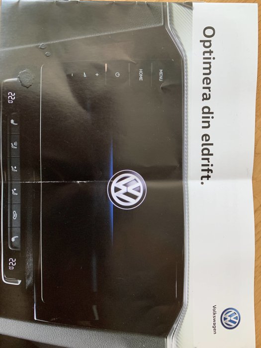 Del av bilens kontrollpanel och en Volkswagen-folder med texten "Optimera din eldrift".