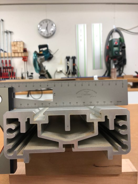 Linjal ligger på tvärs över två identiska metallprofiler för att visa att mitten är något högre än sidorna i en verkstadsmiljö