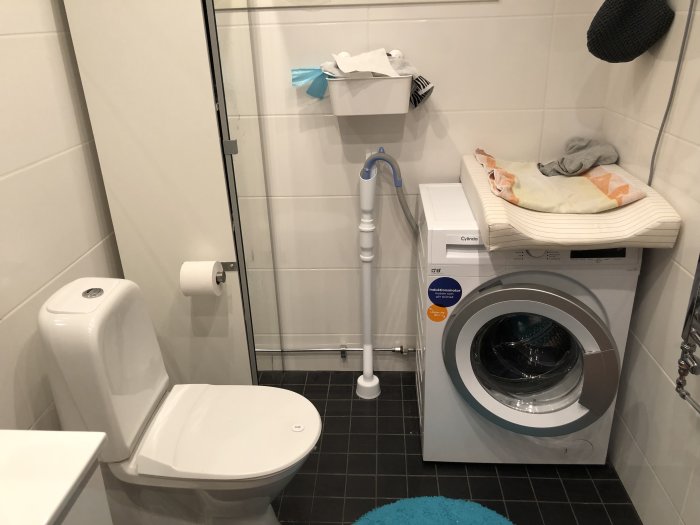 Ett badrum med toalett, tvättmaskin, handfat och en synlig golvbrunn som används för avlopp.