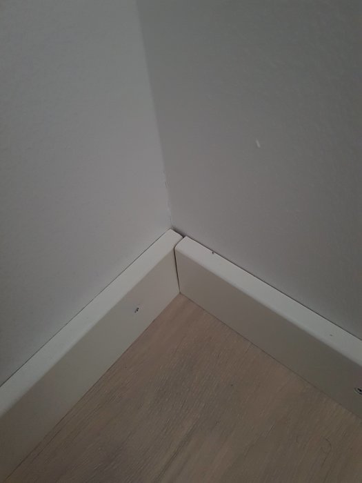 Vitmålade lister i hörn med synliga skruvhuvuden och dåligt utförande.