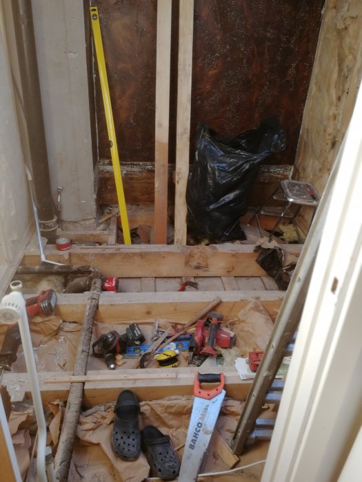 Ongoing renovation with exposed wooden beams, work tools, and black trash bag on the floor.