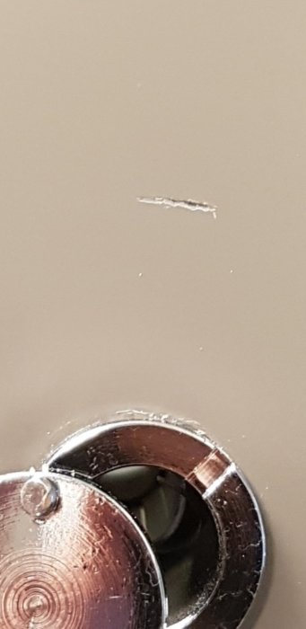 Repa på vägg vid kikhål på dörr, synlig reparation i ögonhöjd.