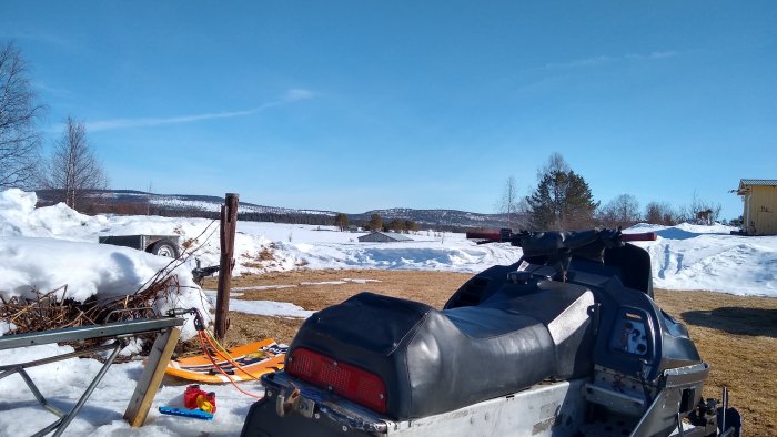 Utsikt över snötäckt landskap med snöskoter i förgrunden och skogklädda kullar i bakgrunden.