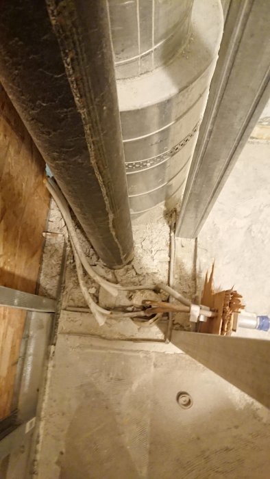 Tappvattenrör och installation nära betonggolv och vägg med synlig isolering och ledningar.