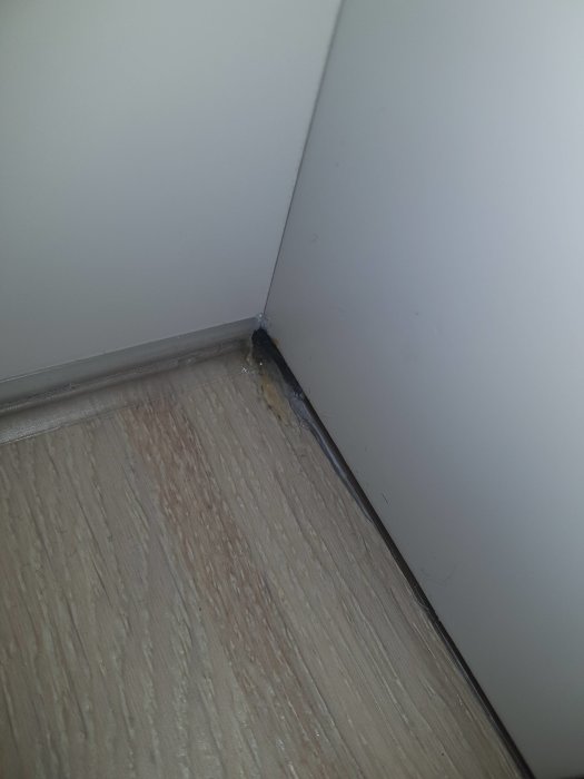 Skadat parkettgolv vid en vägg, synligt lagat med mörkare substans i hörnet.