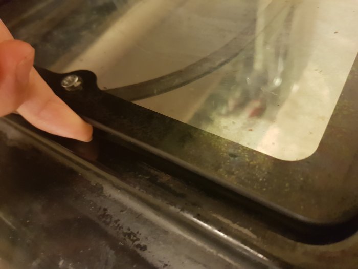 Hand som håller en demonterad ugnslucka med synliga skadade spikar och separerade glaspaneler.