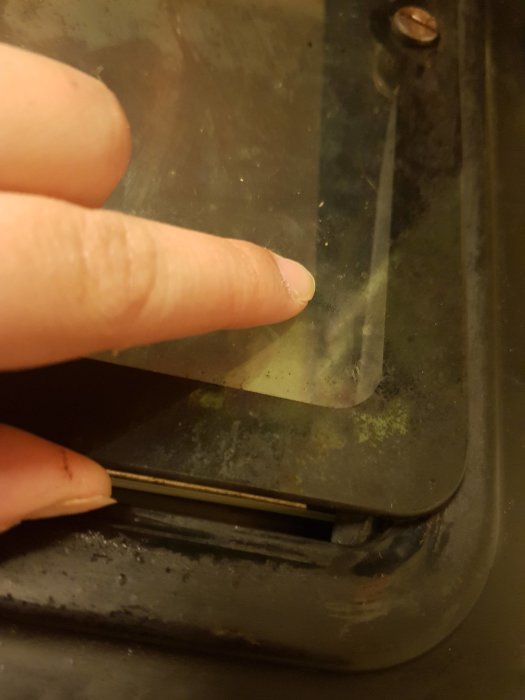 Närbelägen bild på en person som pekar på trasig spik och avbruten fästpunkt mellan två ugnsglas.