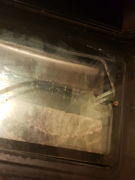 Ugnslucka med lösgjorda innerglas och en bruten spik synlig i hörnet.