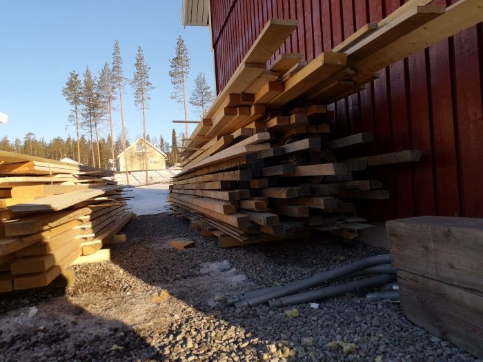 Staplar av träreglar och panel som förvaras utomhus lutade mot en byggnad.