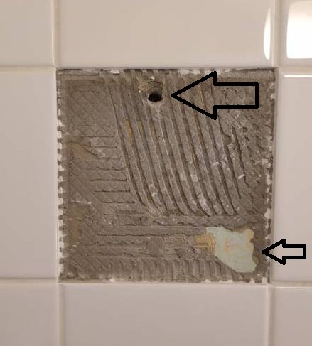 Kakelvägg med ett område där kaklet har tagits bort och visar underliggande byggmaterial.