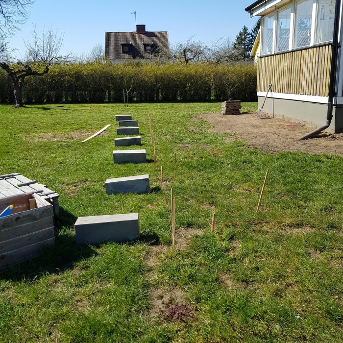 Bild av en trädgård med nylagda plintar i en rad, träreglar på marken och en hög med makadam i bakgrunden.