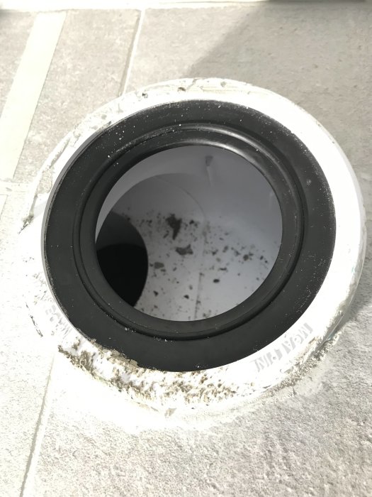 Närbild på ett vitt rörgenomföringshål med en svart packning, orosanmärkning om installation.
