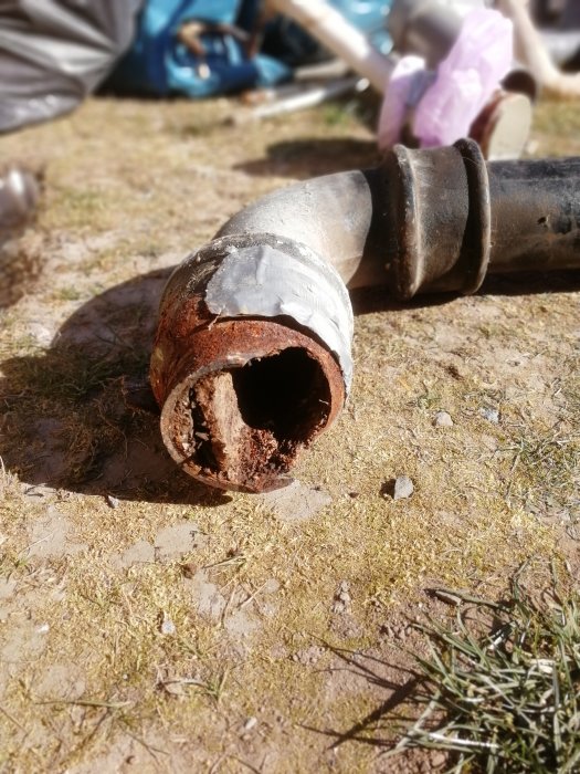 Närbild på ett rostigt och igensatt avloppsrör på marken, tecken på slitage och behov av byte.