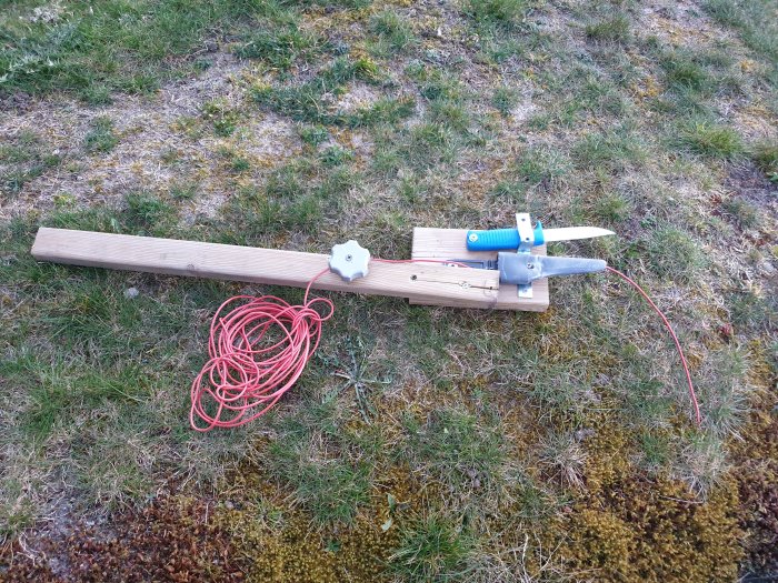 Handgjord träprototyp för trädgårdsarbete på gräsmatta med sprucket virke och röd lina.