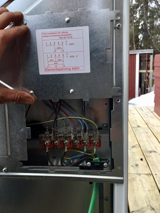 En öppen spispanel med elanslutningar och en installationsinstruktion utomhus.