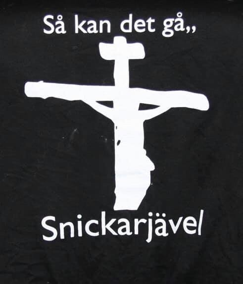 Svart t-shirt med tryck: "Så kan det gå, snickarjävel" och stiliserad bild av person på kors.