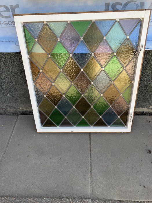 Färgglatt glasfönster med diamantmönster lutat mot en vägg på en trottoar.