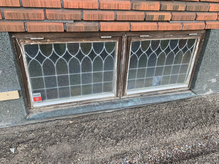 Oputsade källarfönster med bågformade rutor under en tegelvägg.