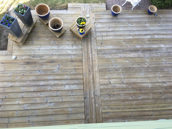 Obehandlad träveranda tvättad med högtryckstvätt, med blomlådor och krukor runtomkring.