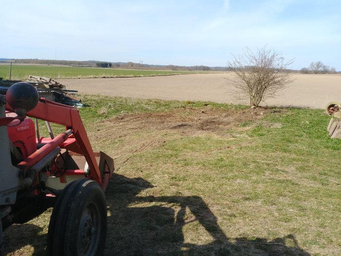 Rensad yta på lantgård, traktorförare och åker i bakgrunden, hög med gammalt material till vänster.