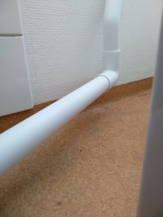 Vit rörinstallation som löper längs med ett hörn på väggen nära golvet.