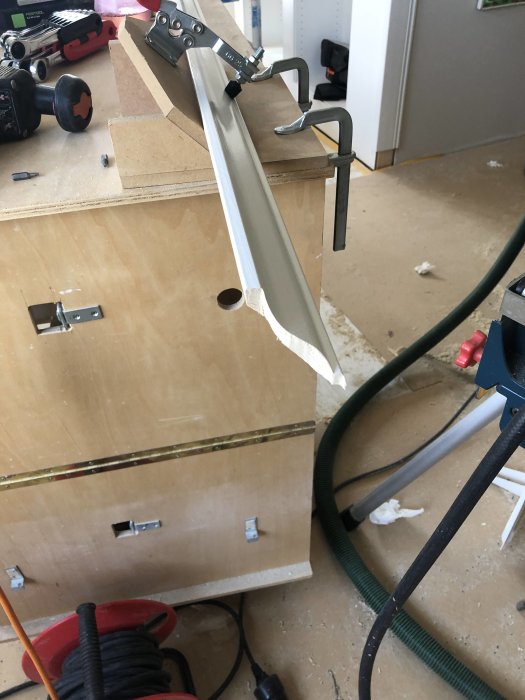Listverk fastsatt med klämmor på arbetsbänk under beredning, med verktyg och material synliga.