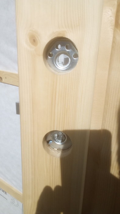 Låscylinder och låskista på en ljus träförrådsdörr, potentiellt för byte till ASSA eller Dorma system.