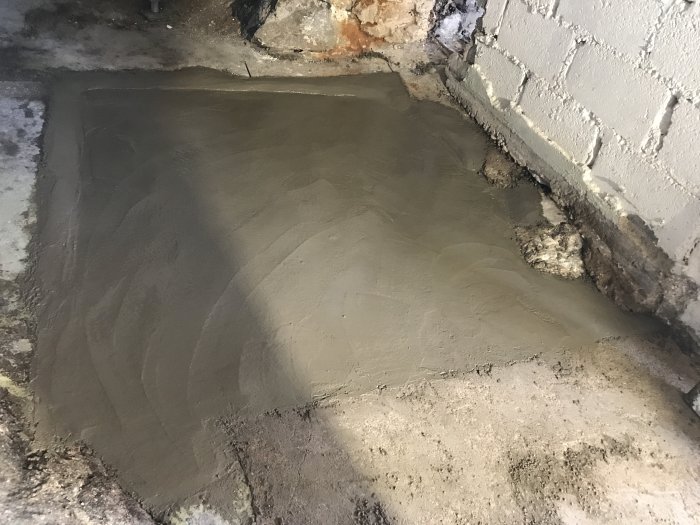 Putsad yta på betonggolv med delvis målad betongvägg till höger.