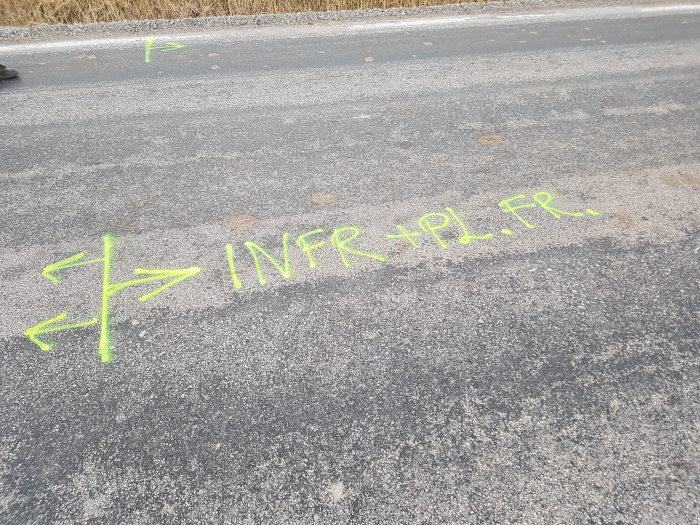 Asfalt med grön markeringstext "INFR + PL.FR." och en pil på en väg som ska renoveras.