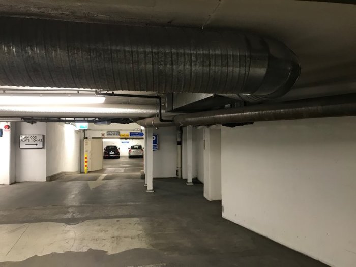 Parkering i garage med synliga rör och en gulsvart avspärrning delvis dold bakom röret.