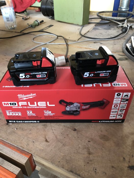 Två nya Milwaukee M18 REDLITHIUM 5.0 Ah batterier ovanpå en kartong för en Milwaukee M18 FUEL verktyg.