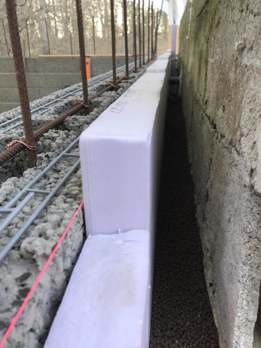 Isolering med frigolit längs en poolvägg med armeringsjärn och Lecakulor för byggprojekt.